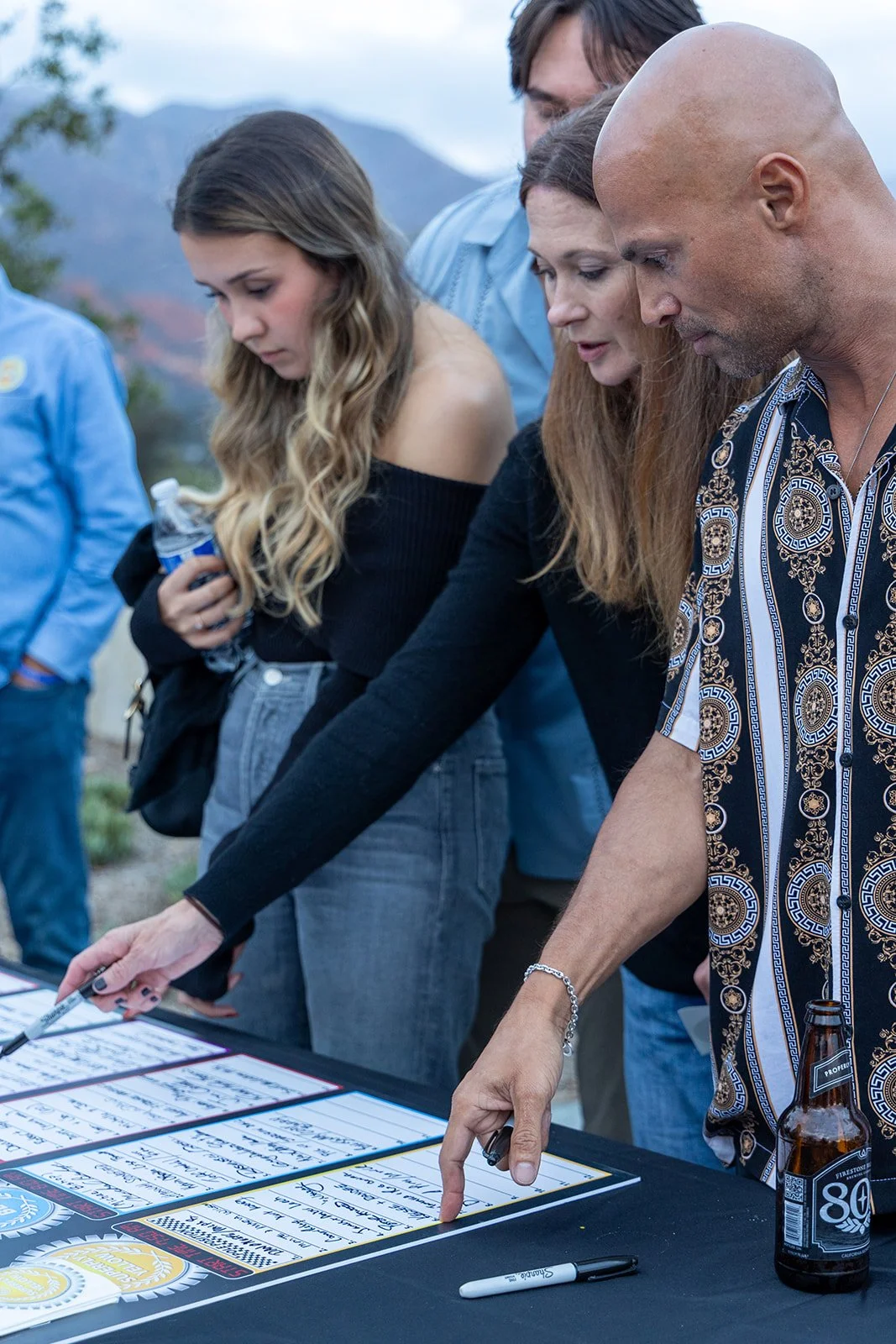 Group of people signing posters or photographs at an outdoor event.