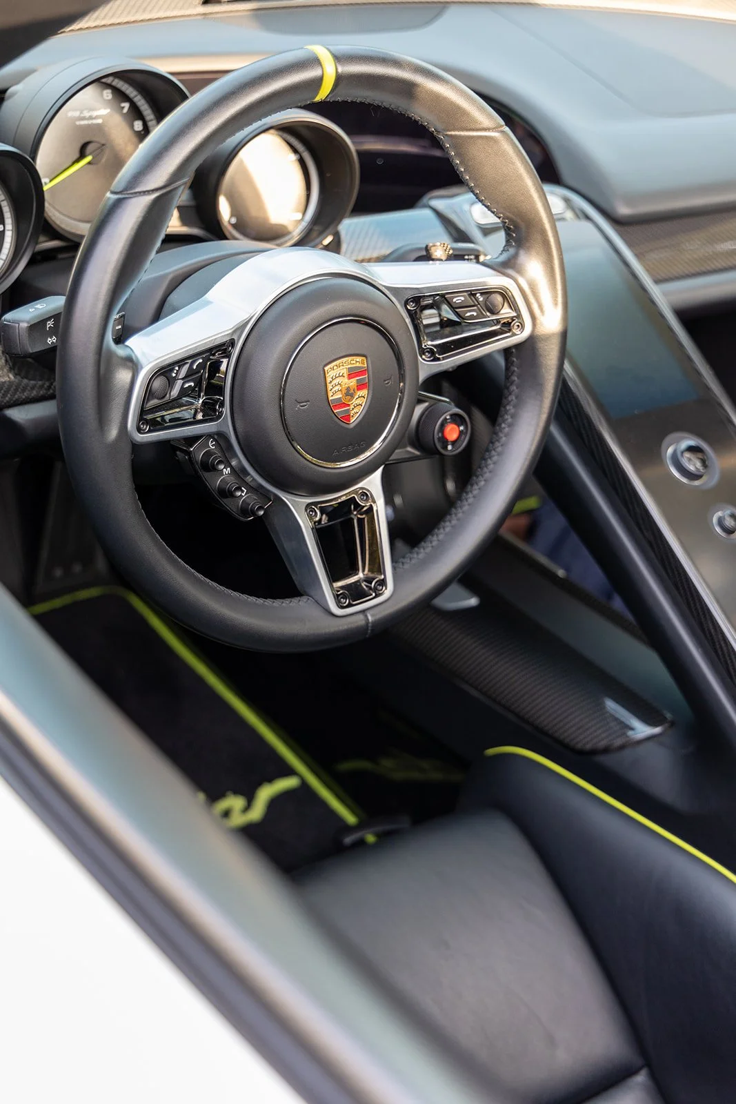 Interior of a Porsche sports car showing the steering wheel with Porsche logo, part of the dashboard, and racing seat with yellow accents.