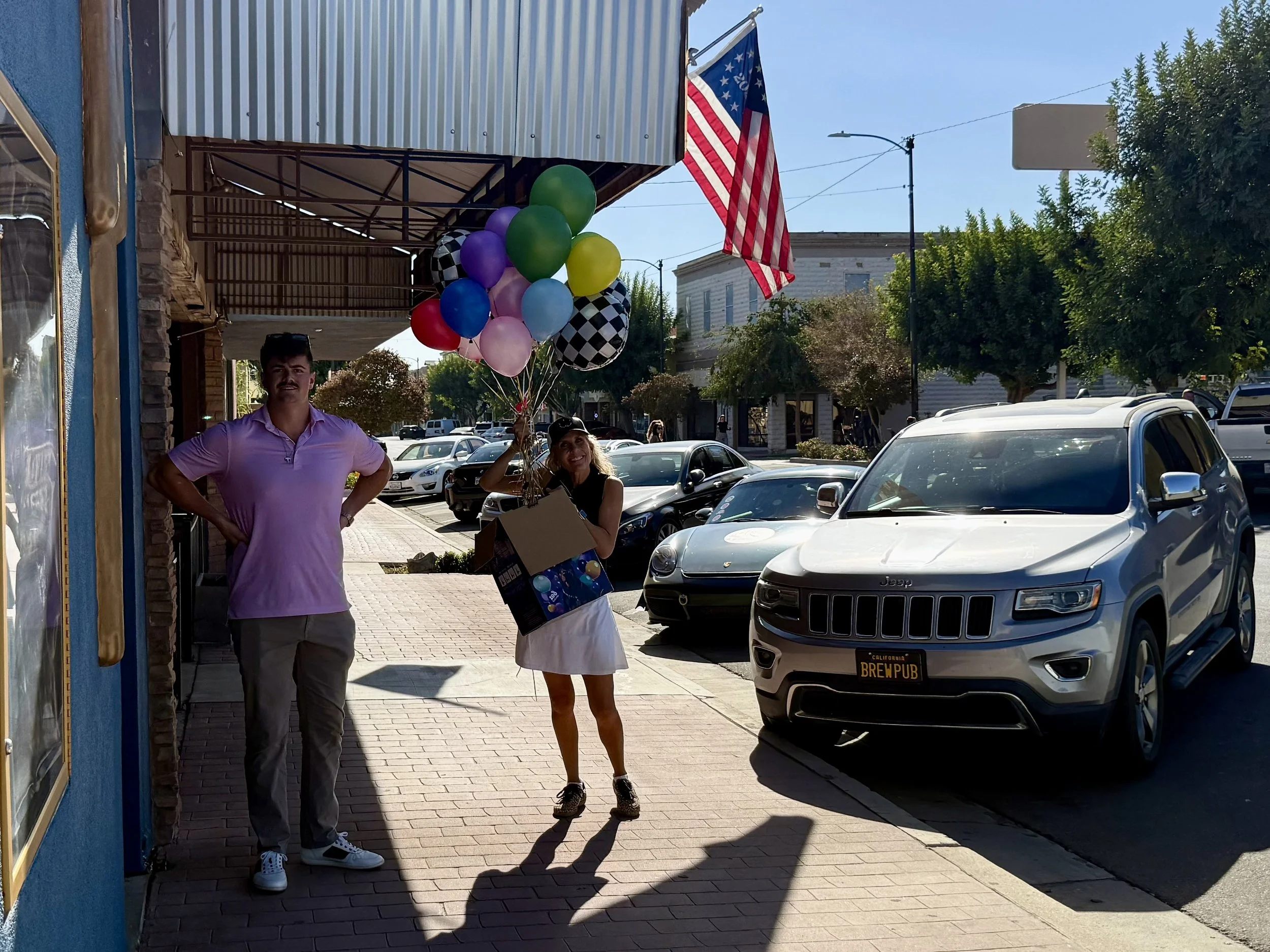 man-in-pink-shirt-and-woman-holding-balloons-on-sidewalk--eb2b88eb.jpeg