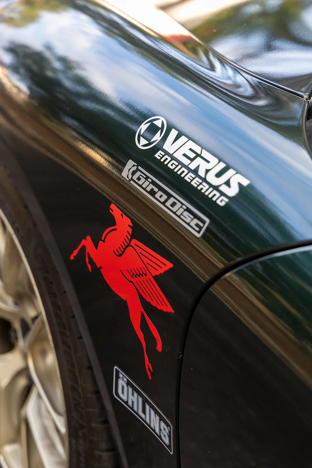 Close-up of a car with various stickers, including the logos of Vexus Engineering, Microdisc, a red Pegasus decal, and a Stilling sticker.
