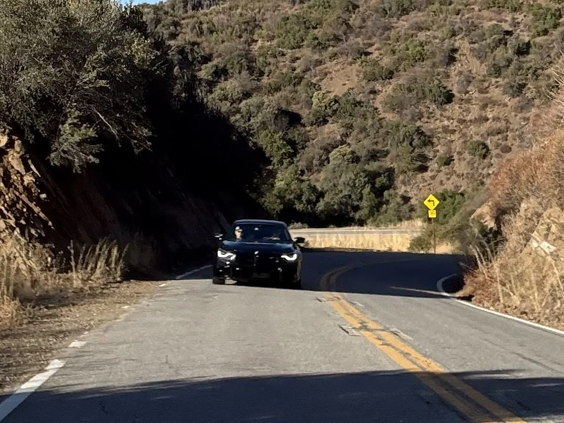 black-car-driving-on-winding-mountain-road-with-yellow-sign--607a7c88.jpeg