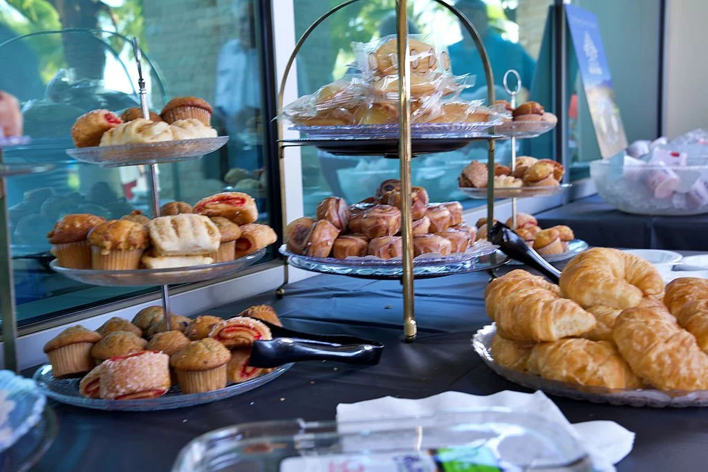 Assorted pastries including croissants, muffins, and Danishes displayed on tiered trays and plates at a bakery or cafe.