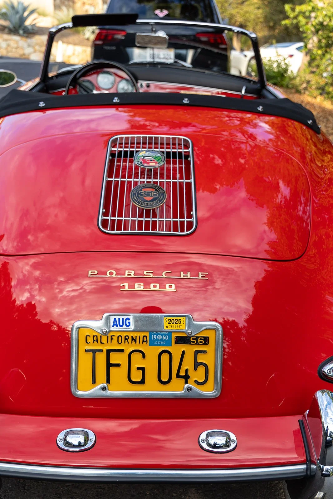 Red vintage Porsche 1600 convertible with California license plate TFG 045, showing a hood vent, badges, and a black folded soft top, parked outdoors.