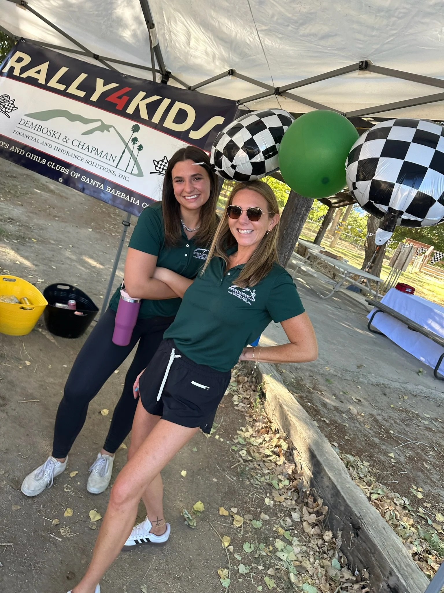 two-women-in-green-shirts-pose-under-a-tent-with-checkered-balloons--525098db.jpeg