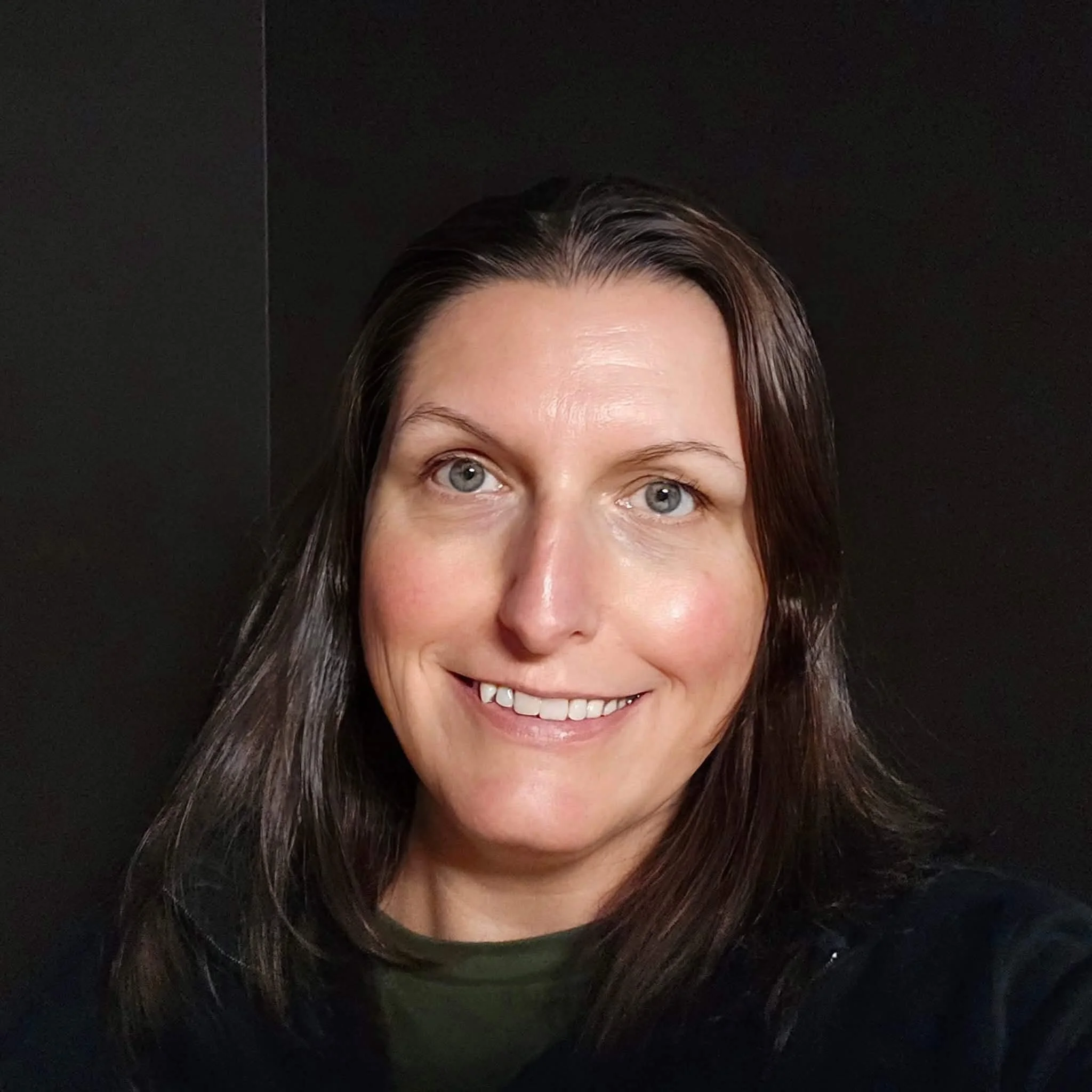 Partially visible woman with light skin, straight brown hair, and bright blue eyes smiling against a black background.