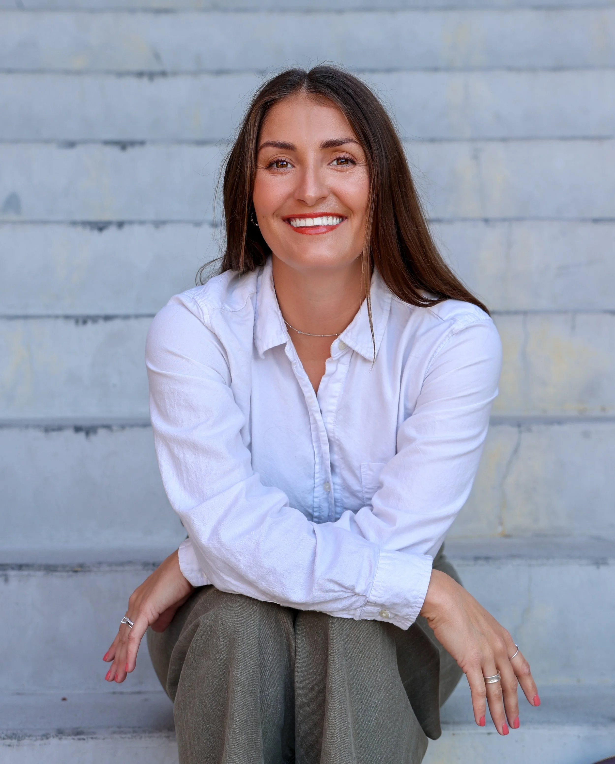 Jessica Clark smiling, wearing a white shirt, sitting on concrete stairs.
