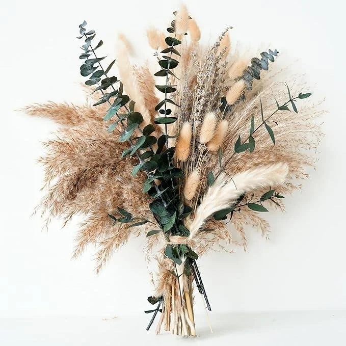 A bouquet of dried pampas grass and eucalyptus leaves against a plain white background.