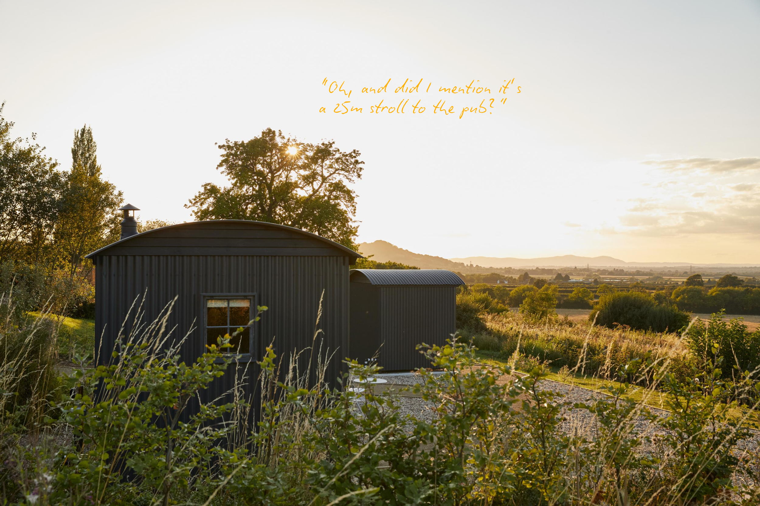 Photo of a rural landscape at sunset with a small dark building in the foreground, rolling hills in the distance, trees, and a sky with clouds. Text overlay says, 'Oh, and did I mention it’s a 25m stroll to the pub?'
