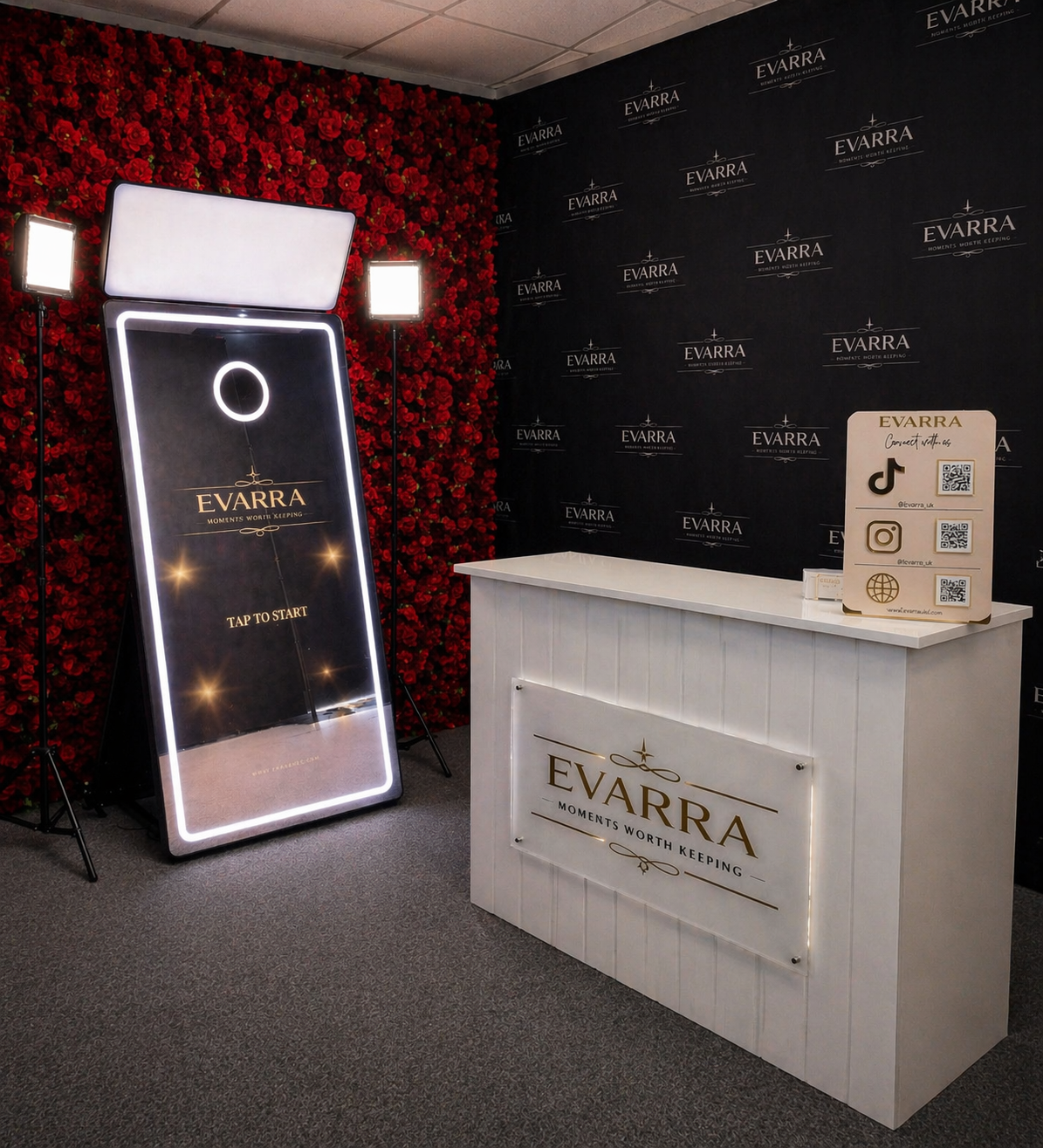 A reception area for Evarra with a white desk, logo, and a digital sign, set against a backdrop of red roses and a black wall with the Evarra logo.