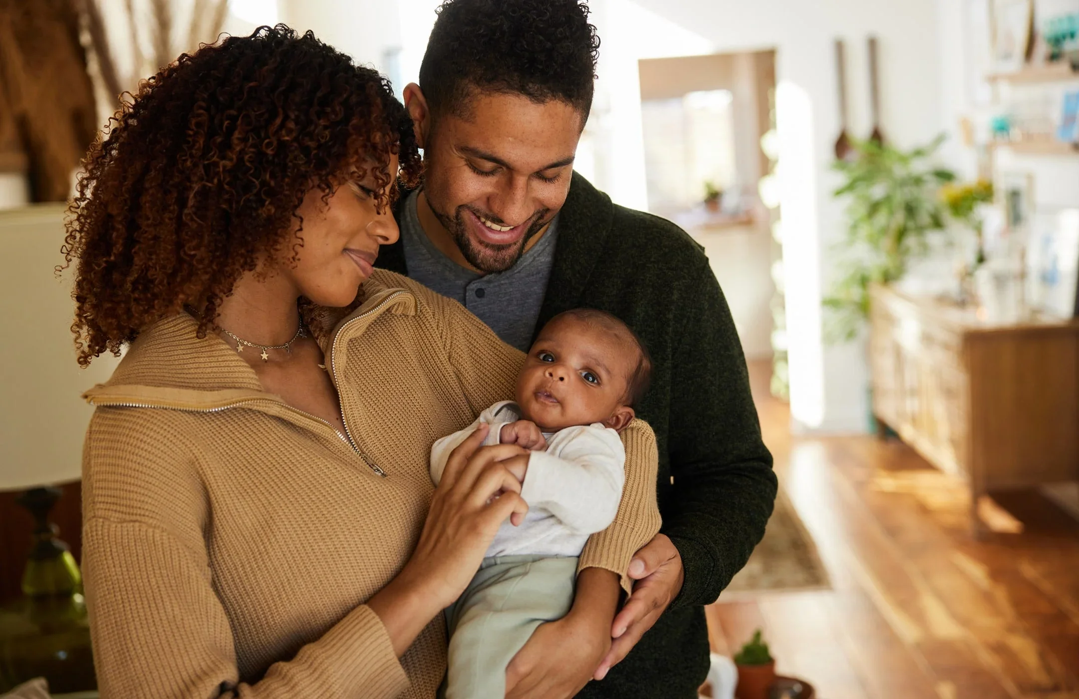 A family of three holding a baby in a cozy, well-lit home.