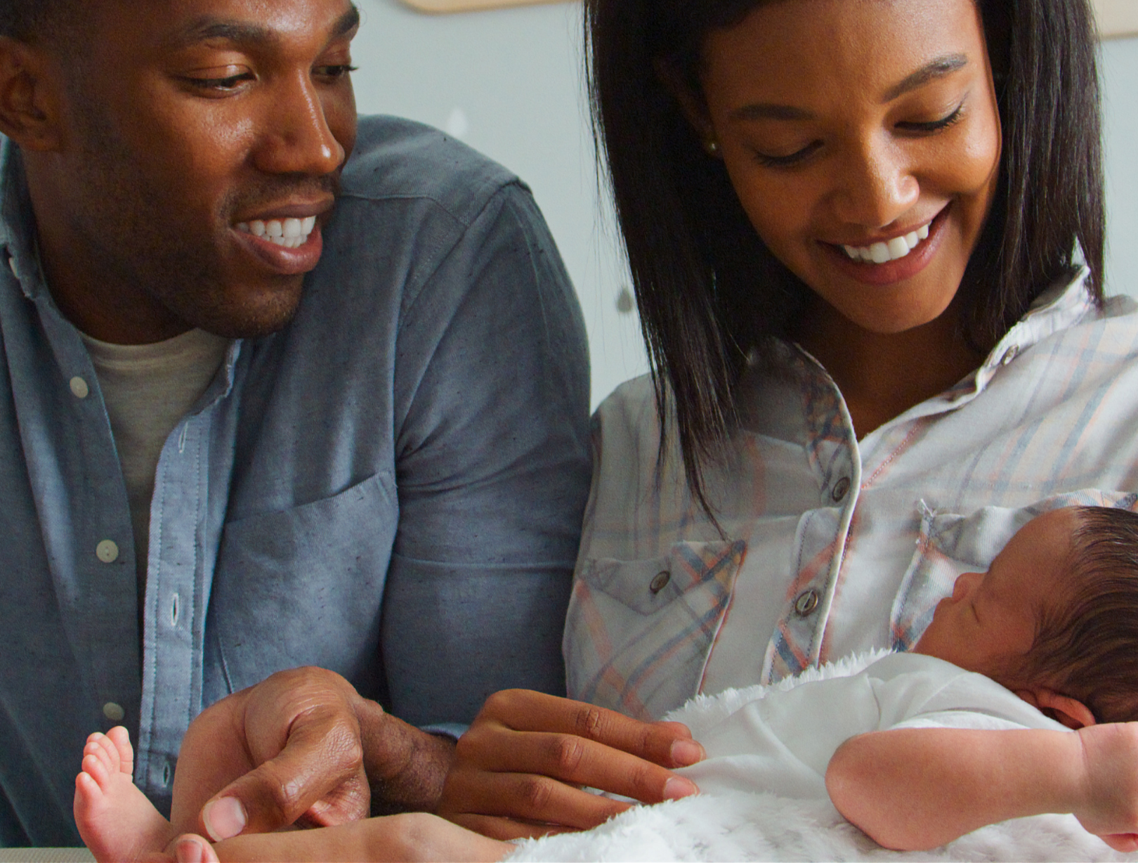 A man and woman smiling while holding a newborn baby in their arms.