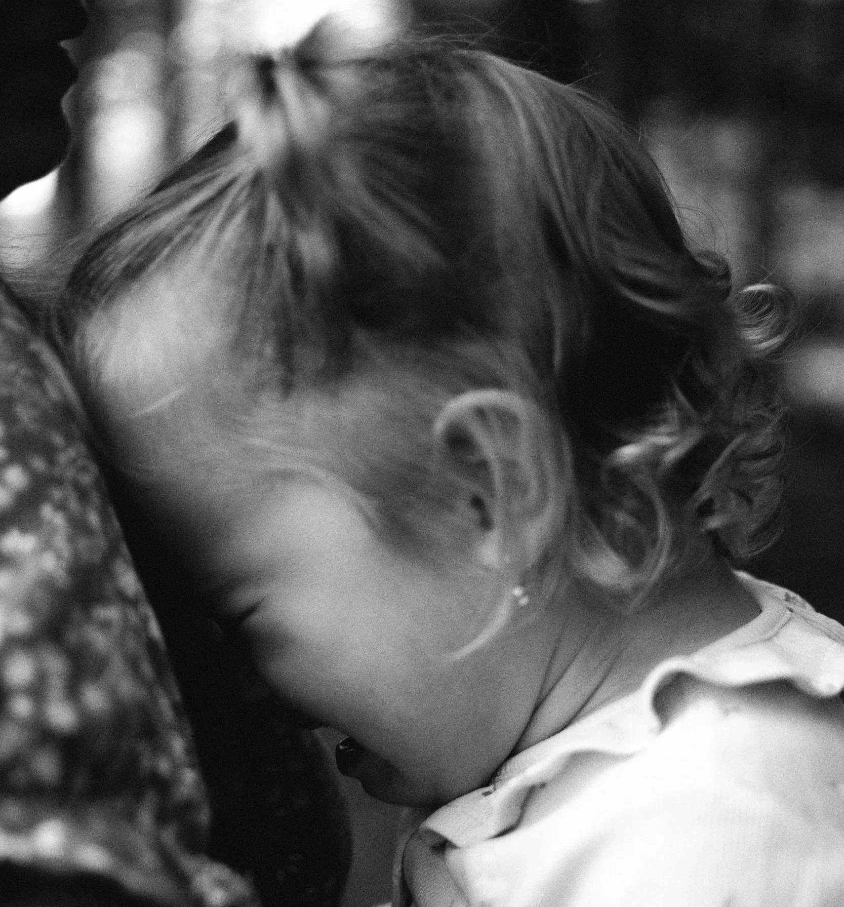 Black-and-white photo of a toddler burying her face against a caregiver’s shoulder, expressing emotional overwhelm. Represents the intensity of toddler tantrums and the importance of connection-first parenting strategies.