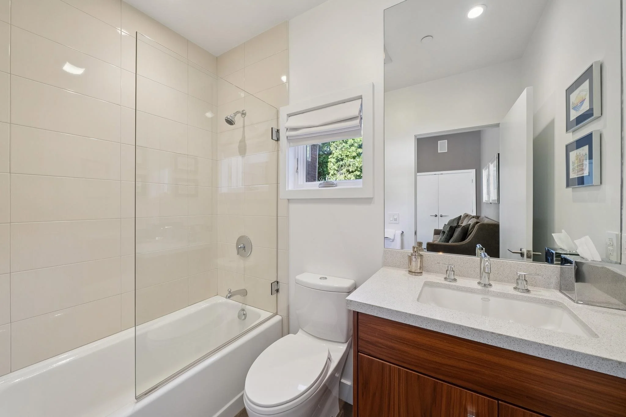 Bathroom with bathtub and shower, white toilet, and vanity with a sink, a mirror, and framed artwork on the wall.