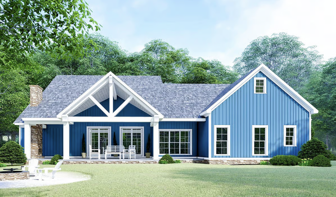 Blue house with gabled roof, sitting on a green lawn surrounded by trees, with white trim and a stone foundation.