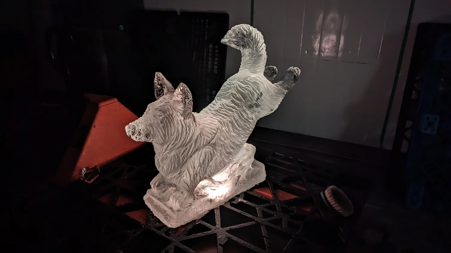 Ice sculpture of two dogs on a wheeled cart in a dimly lit room.