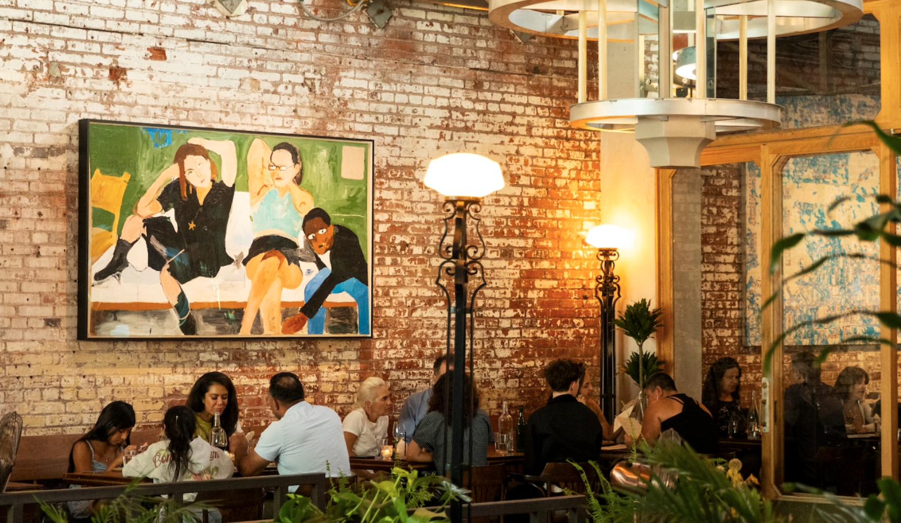 People dining in a restaurant with exposed brick walls, black lamp posts, and colorful artwork on the wall.