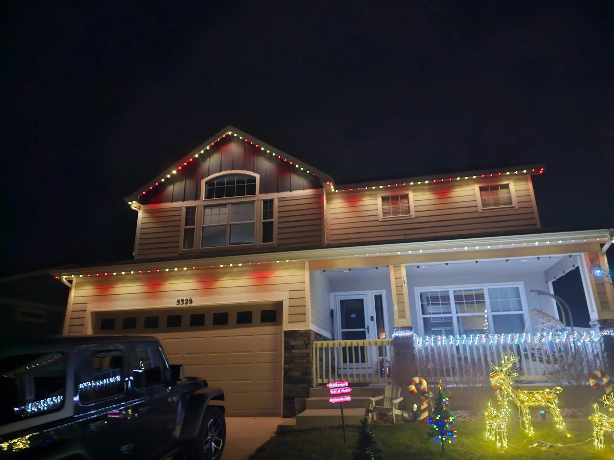 Suburban house decorated with Christmas lights and holiday decorations at night.
