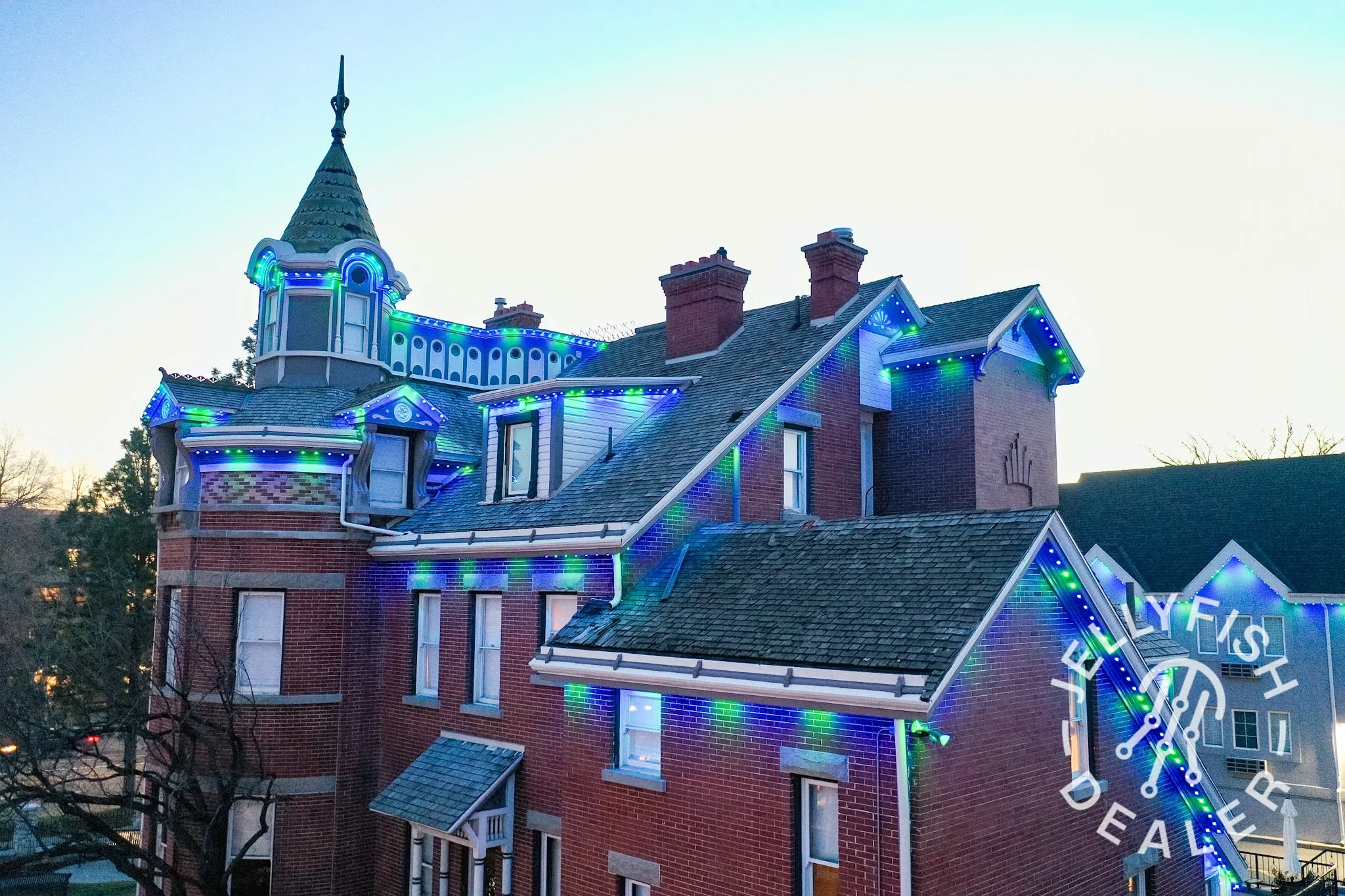 A colorful house decorated with blue and green holiday lights against a twilight sky.