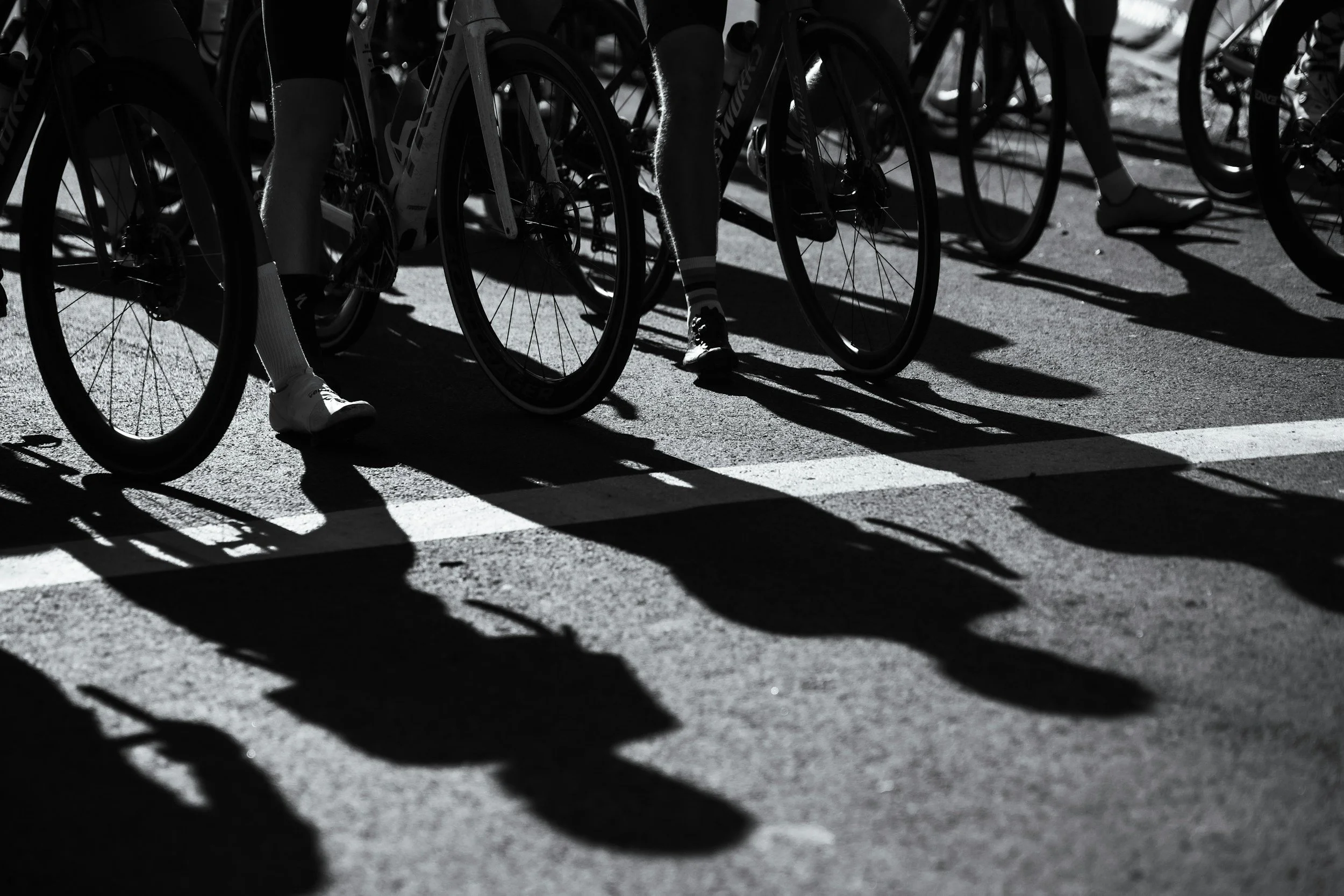Bicycles at start line with runners' legs visible, casting long shadows on pavement during a race.
