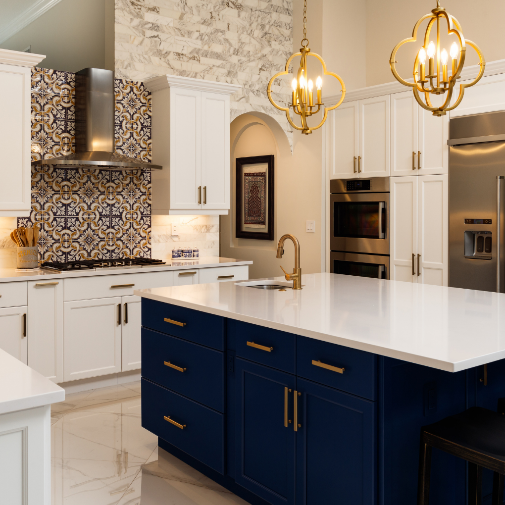 Modern kitchen with white cabinets, a navy blue island with gold hardware, a white quartz countertop, stainless steel appliances, decorative pendant lights, and a patterned tile backsplash.