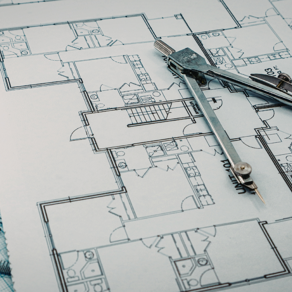 Architectural blueprint of a building with metal compasses placed on top.