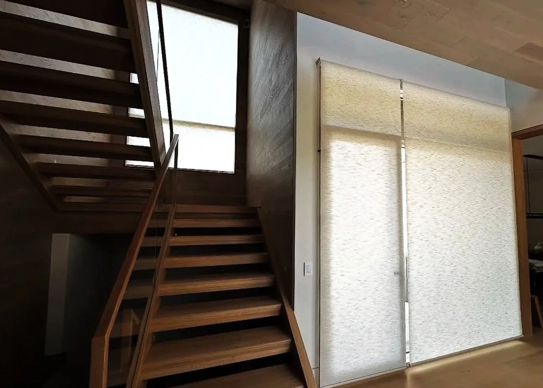 Interior view of a contemporary home featuring a wooden staircase and a sliding fabric door with sunlight filtering through.