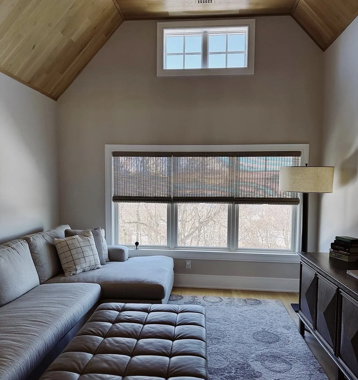 Living room with large window, beige sectional sofa with plaid pillows, wooden ceiling, and a dark wooden media console.