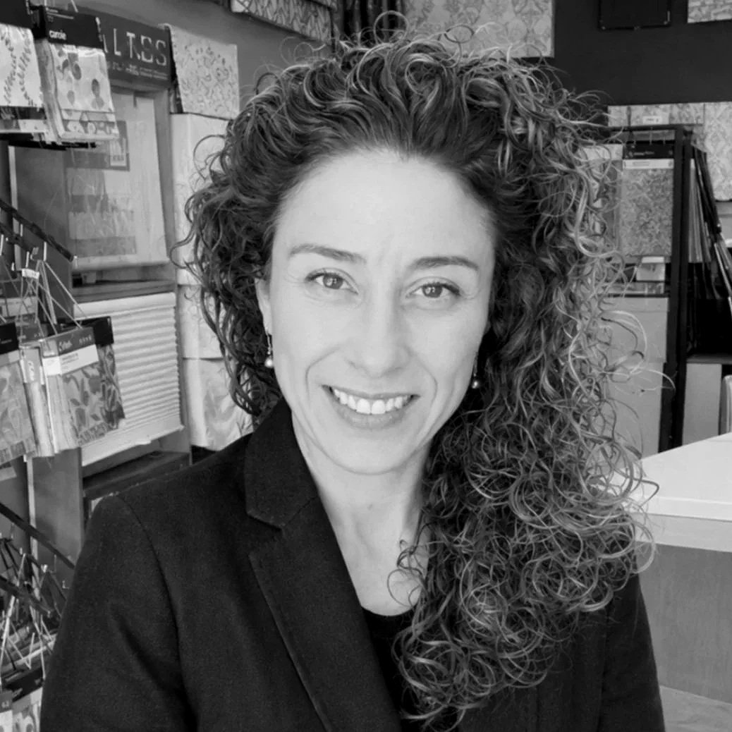 A woman with curly hair and glasses smiling in an indoor setting.