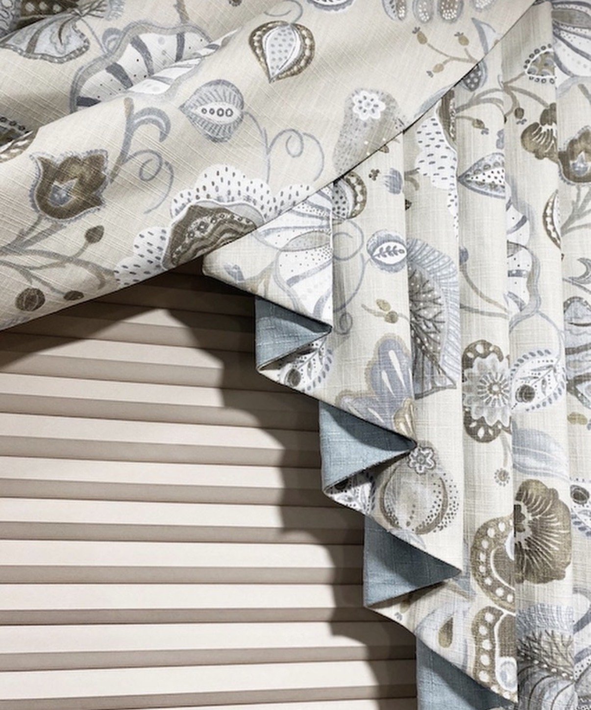 Decorative curtain with floral pattern and pleated valance over beige blinds.