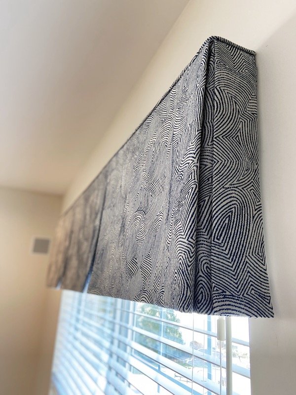 Close-up of a patterned curtain with a geometric design hanging beside window blinds.