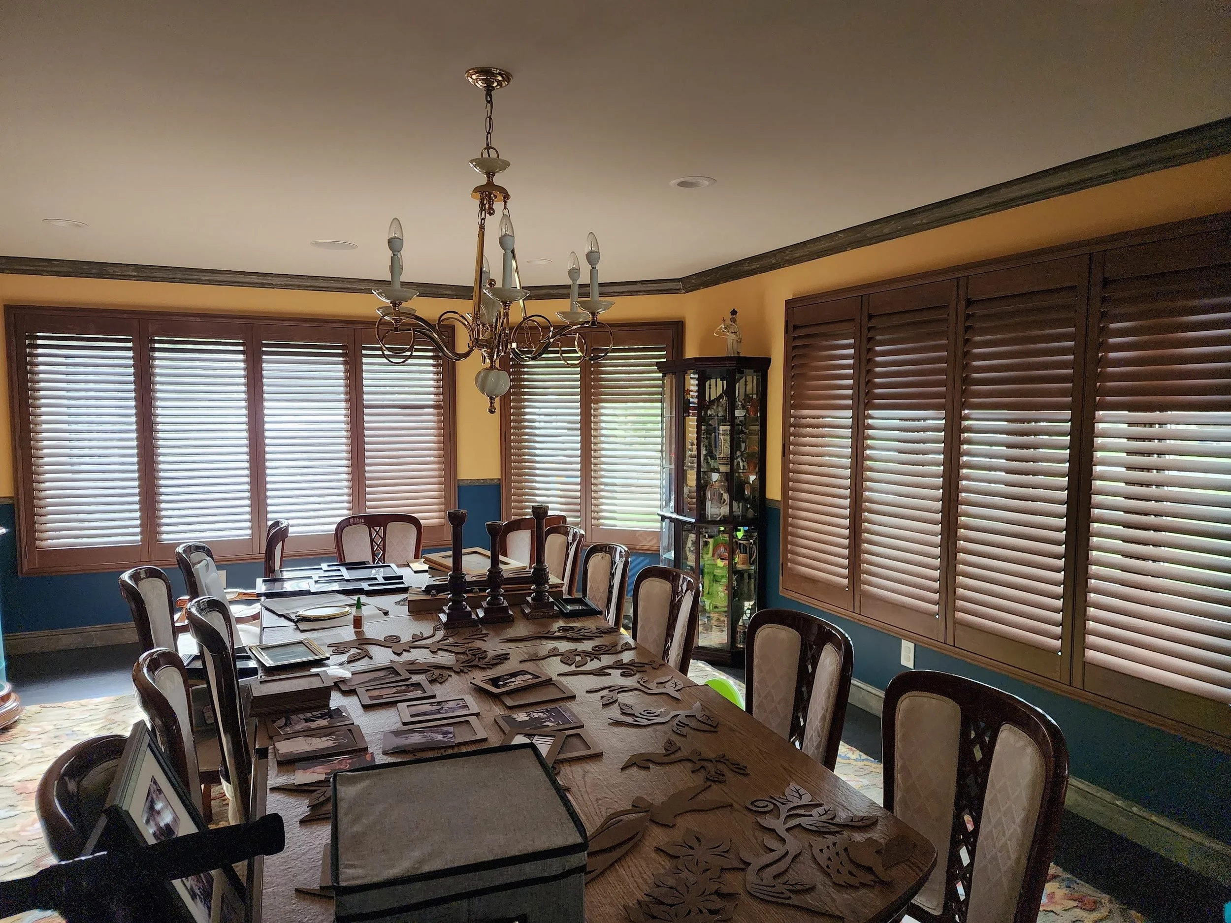 Dining room with wooden table, chairs, window blinds, chandelier, and decorative items.