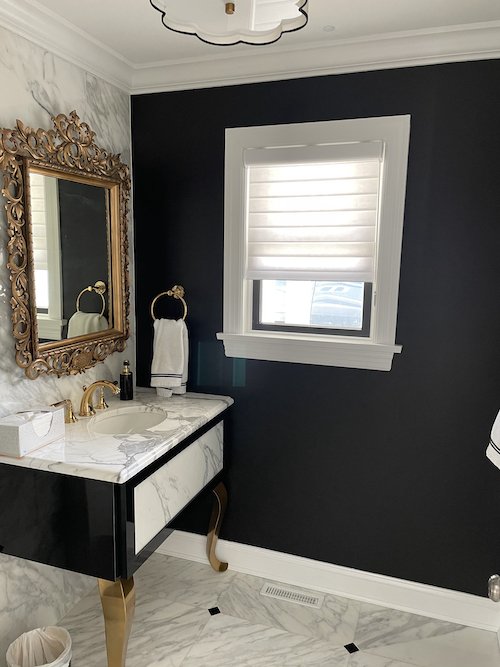 Elegant bathroom with black and white walls, a marble vanity with gold accents, a mirror with ornate gold frame, a window with white blinds, and a marble floor.