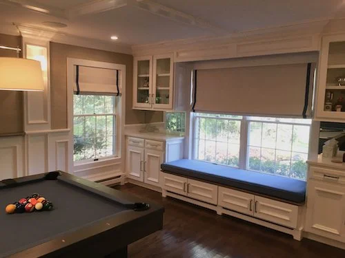 A cozy game room with a pool table and a window seat with a cushion, white cabinetry, and large windows letting in natural light.
