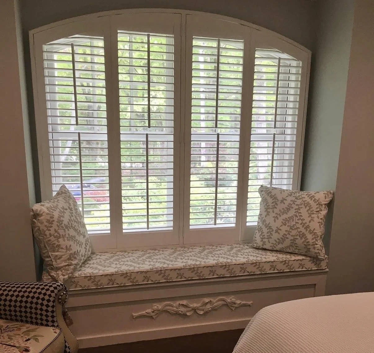Custom white shutters on a large window with seating area.
