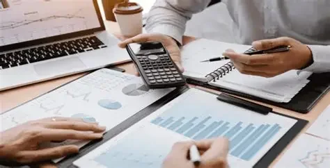 People working with laptops, smartphones, and financial charts for bookkeeping on a desk.