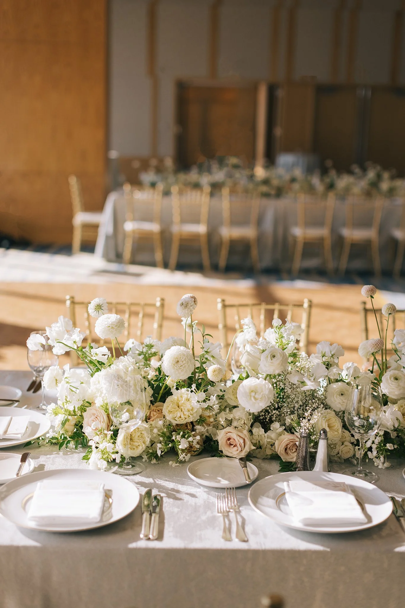Elegant wedding reception table with white floral centerpiece and place settings.