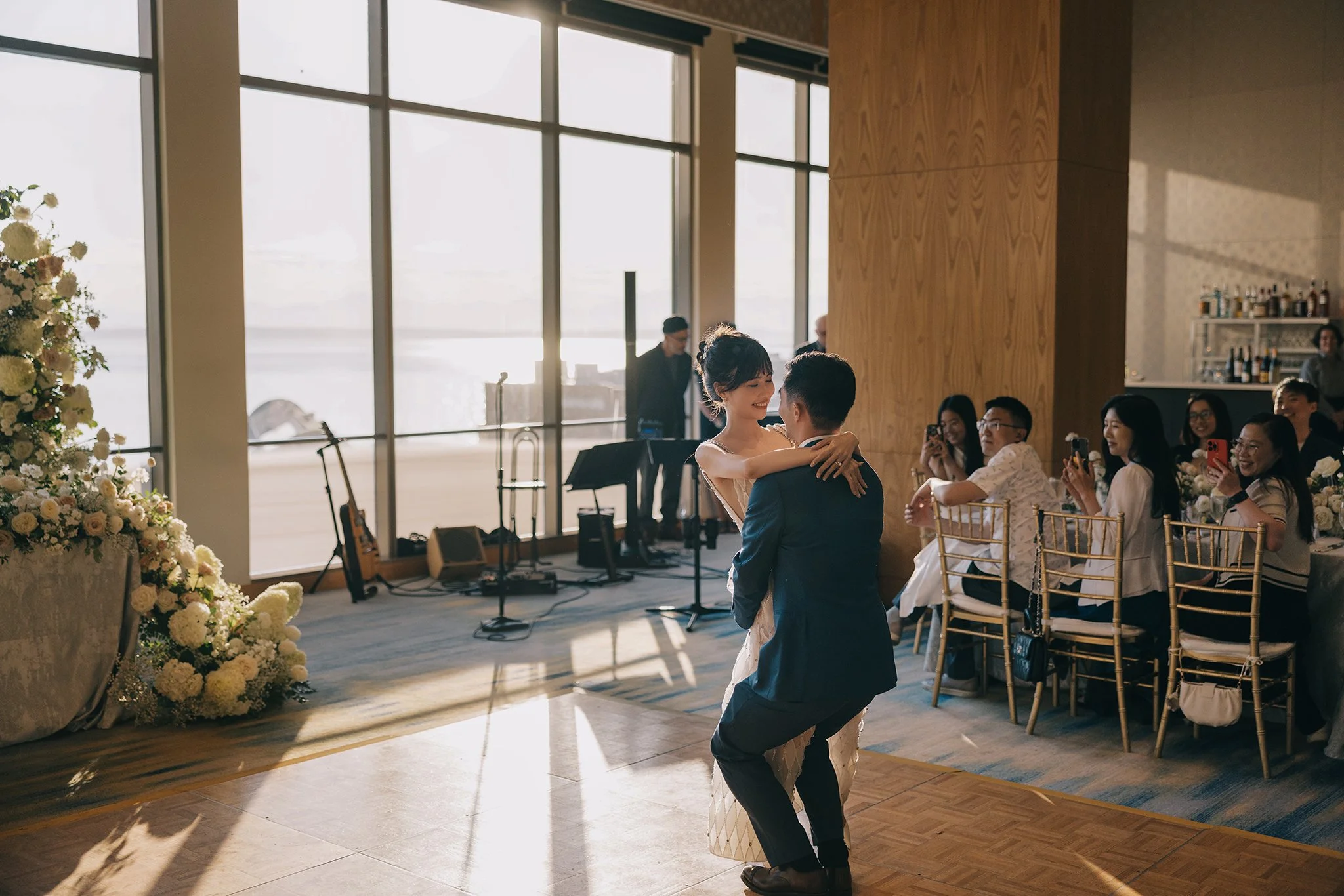 Couple dancing at a wedding reception, with guests seated at tables watching and smiling.
