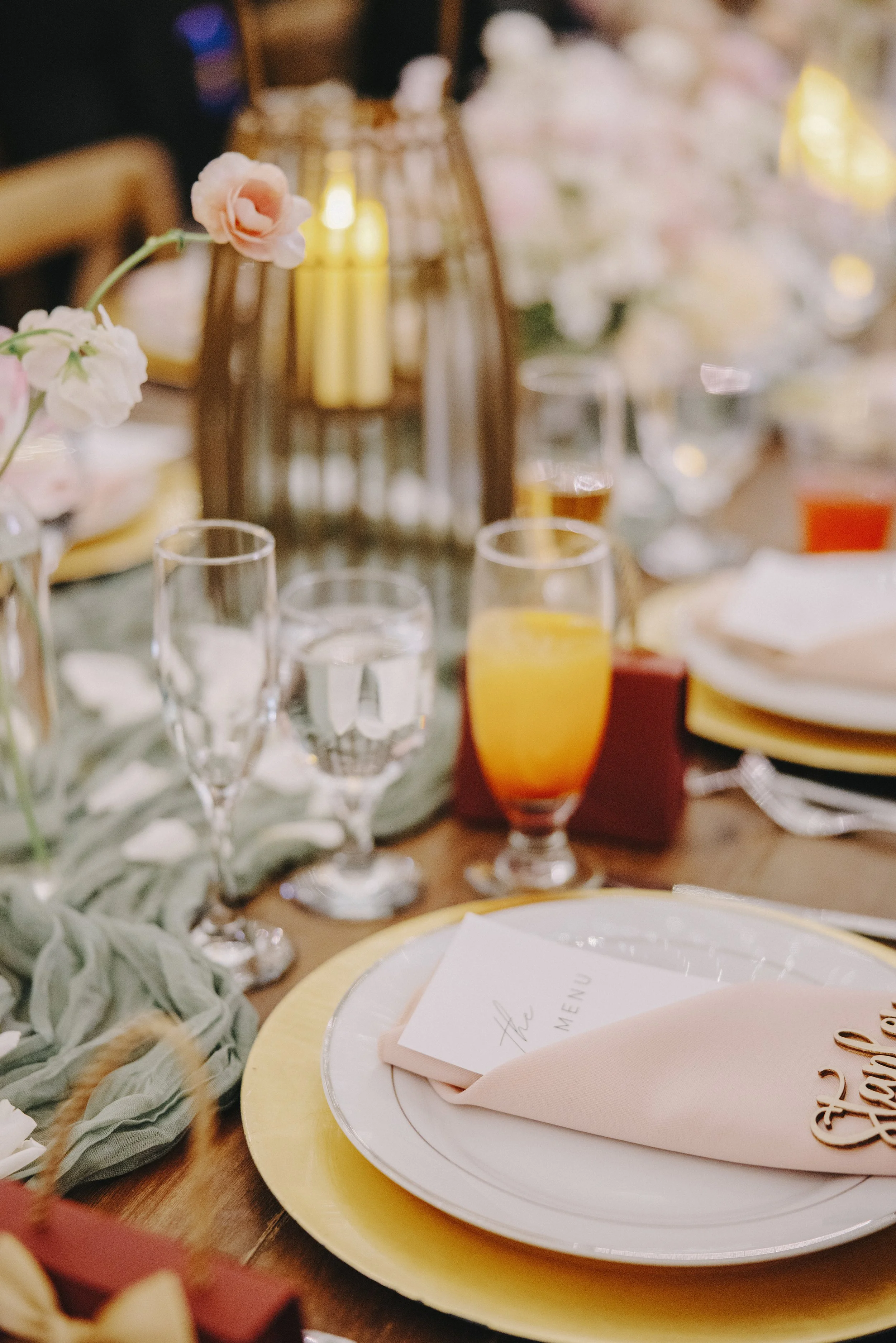 A decorated dining table with flowers, glasses of water and juice, plates, cutlery, and a menu at a formal event.