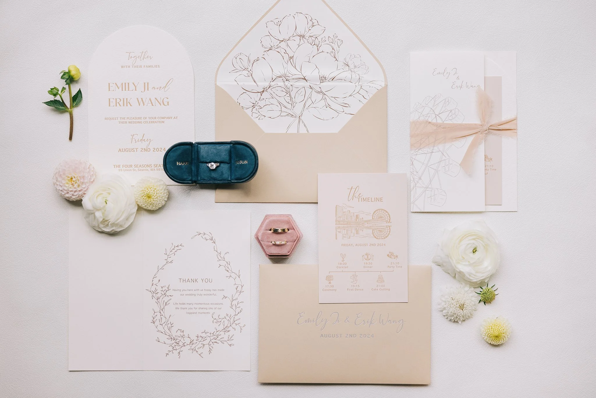 Wedding invitation suite with floral accents, rings in velvet and metal boxes, and flowers on white background.
