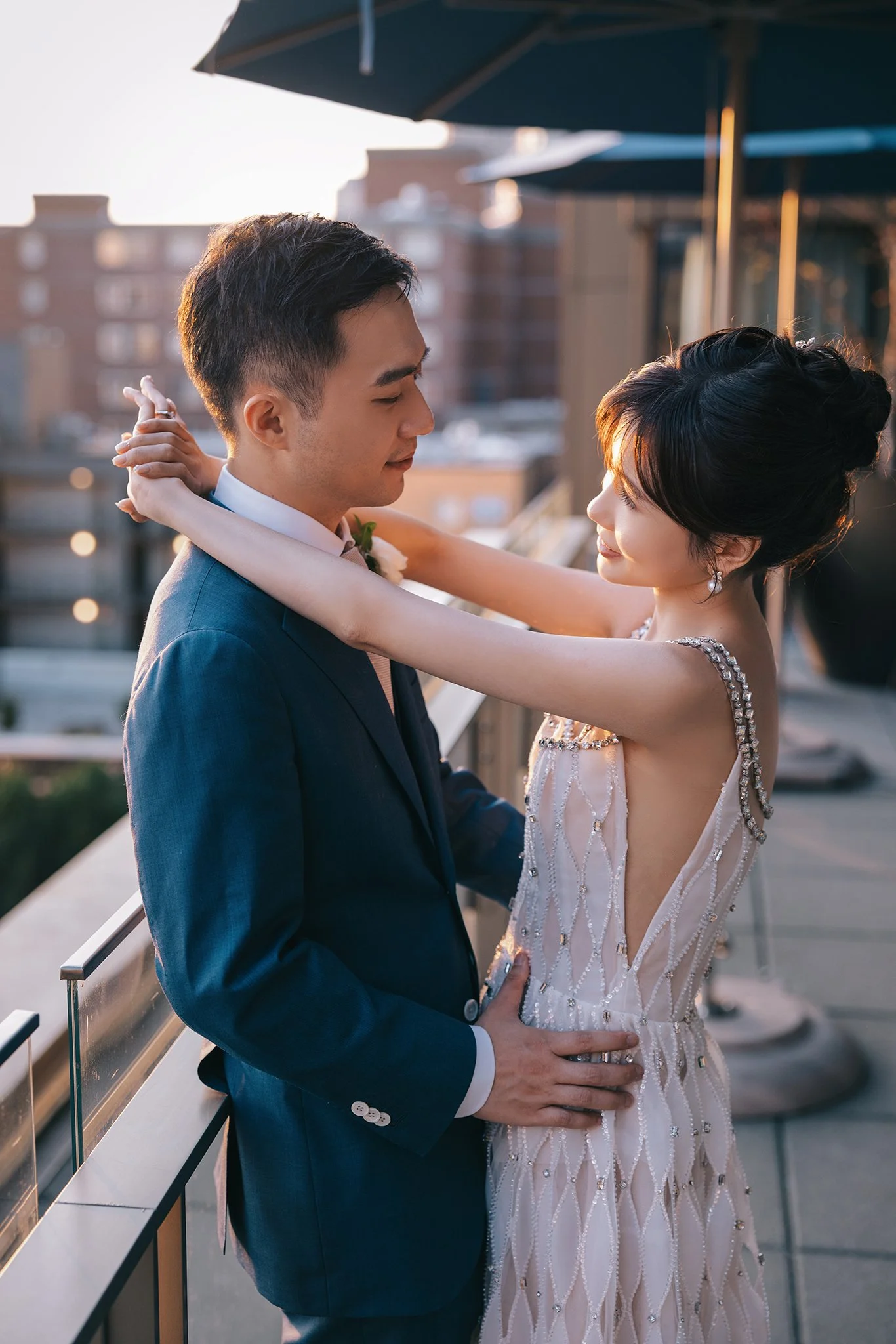 A bride and groom dance together on a rooftop during sunset, with city buildings in the background.