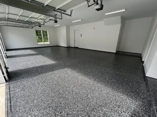 Empty garage with speckled gray epoxy floor, white walls, and a window letting in natural light.
