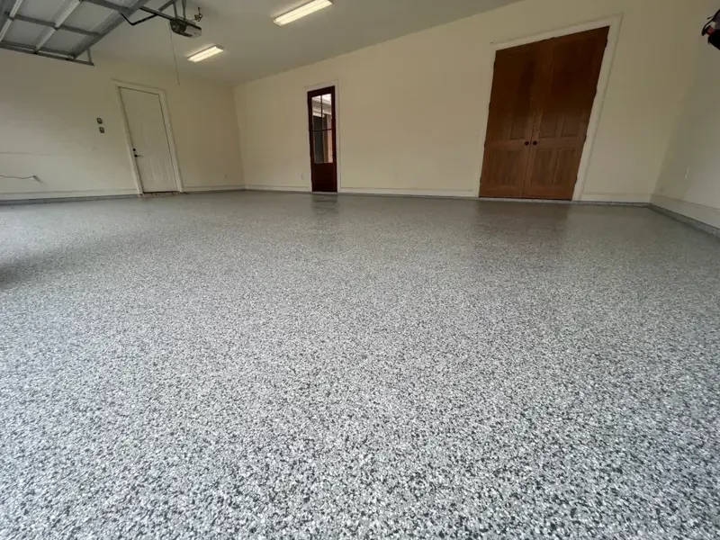 Empty garage with speckled epoxy floor, white walls, and a closed wooden door on the right wall.