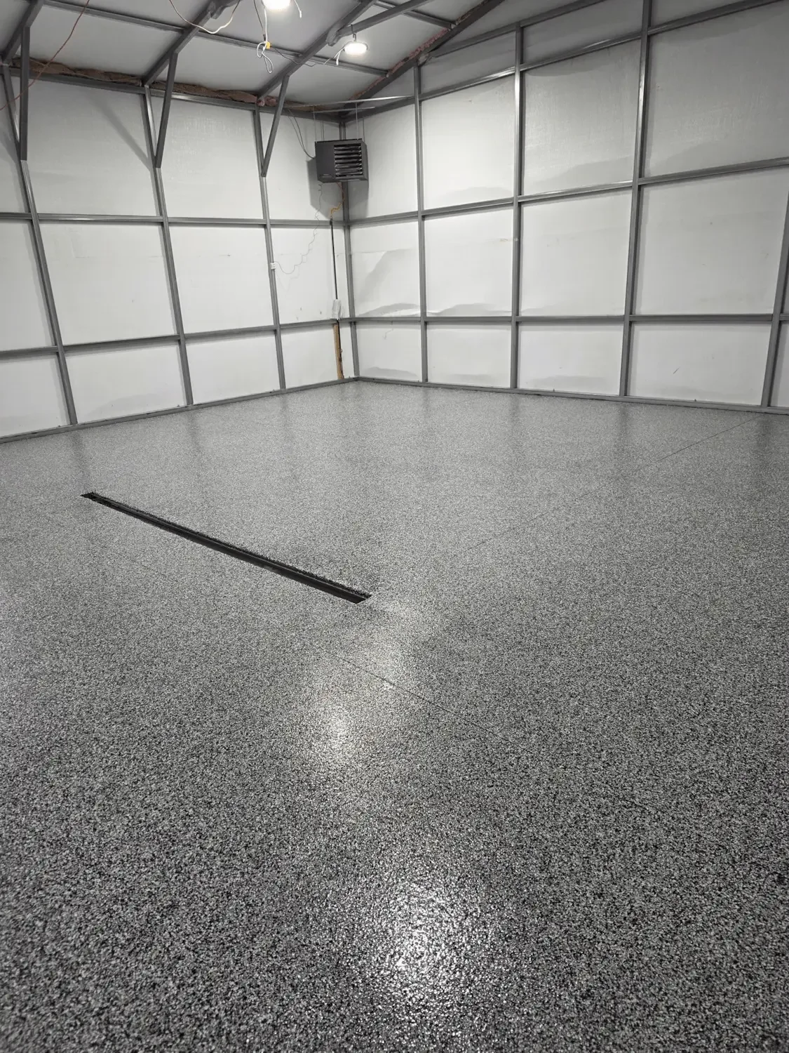 Empty garage with gray textured epoxy floor, metal wall framing, and a wall vent in the corner.