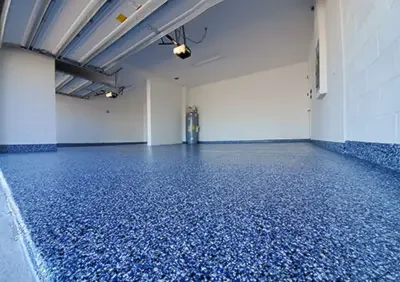Empty indoor garage with blue speckled epoxy floor and white walls, with a fire extinguisher near the back wall.