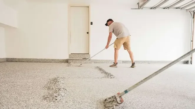 Man spreading new concrete on epoxy garage floor with a long-handled tool