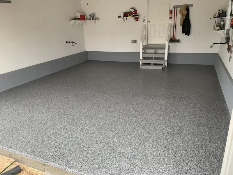 Clean, newly painted garage with gray speckled epoxy floor coating, white walls, and organized shelves with tools and supplies.