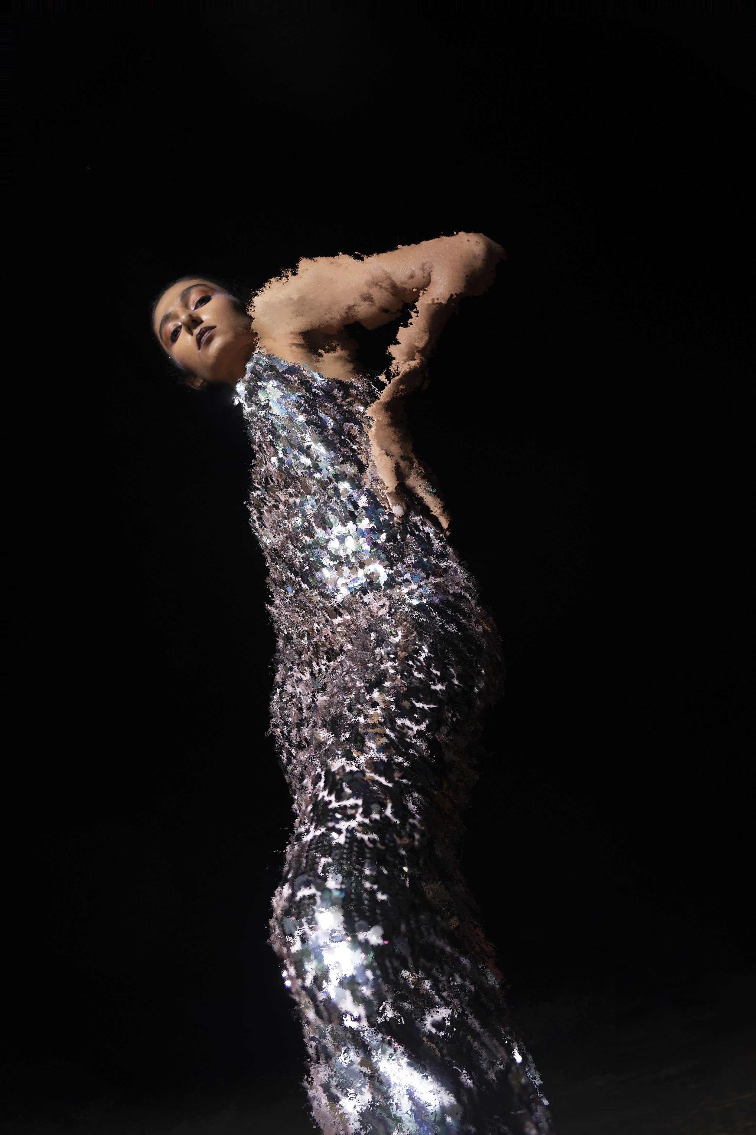 A woman in a shimmering, sequined dress striking a confident pose against a black background.