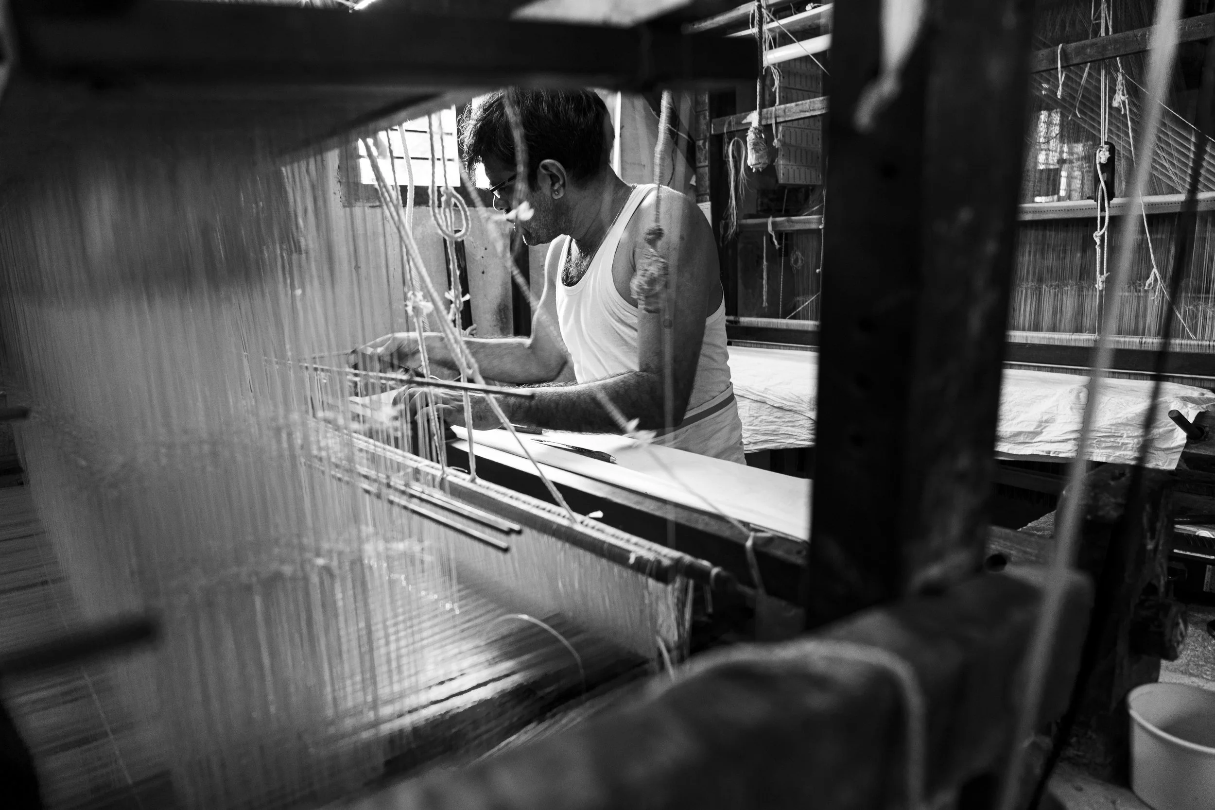 Man weaving on a traditional loom in a workshop, in black and white.