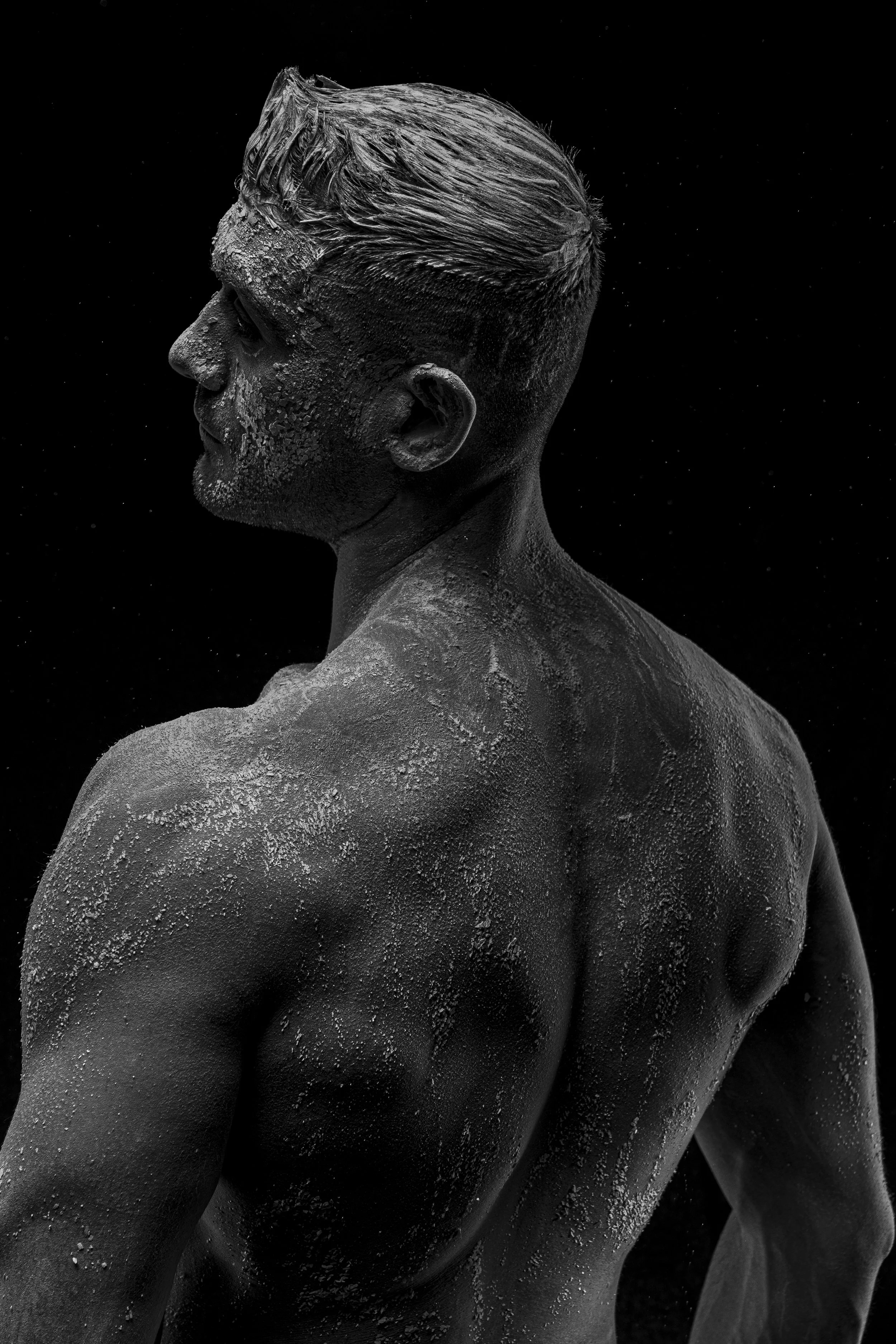 A black and white photo of a man covered in salt, facing left, with a textured look and a dark background.
