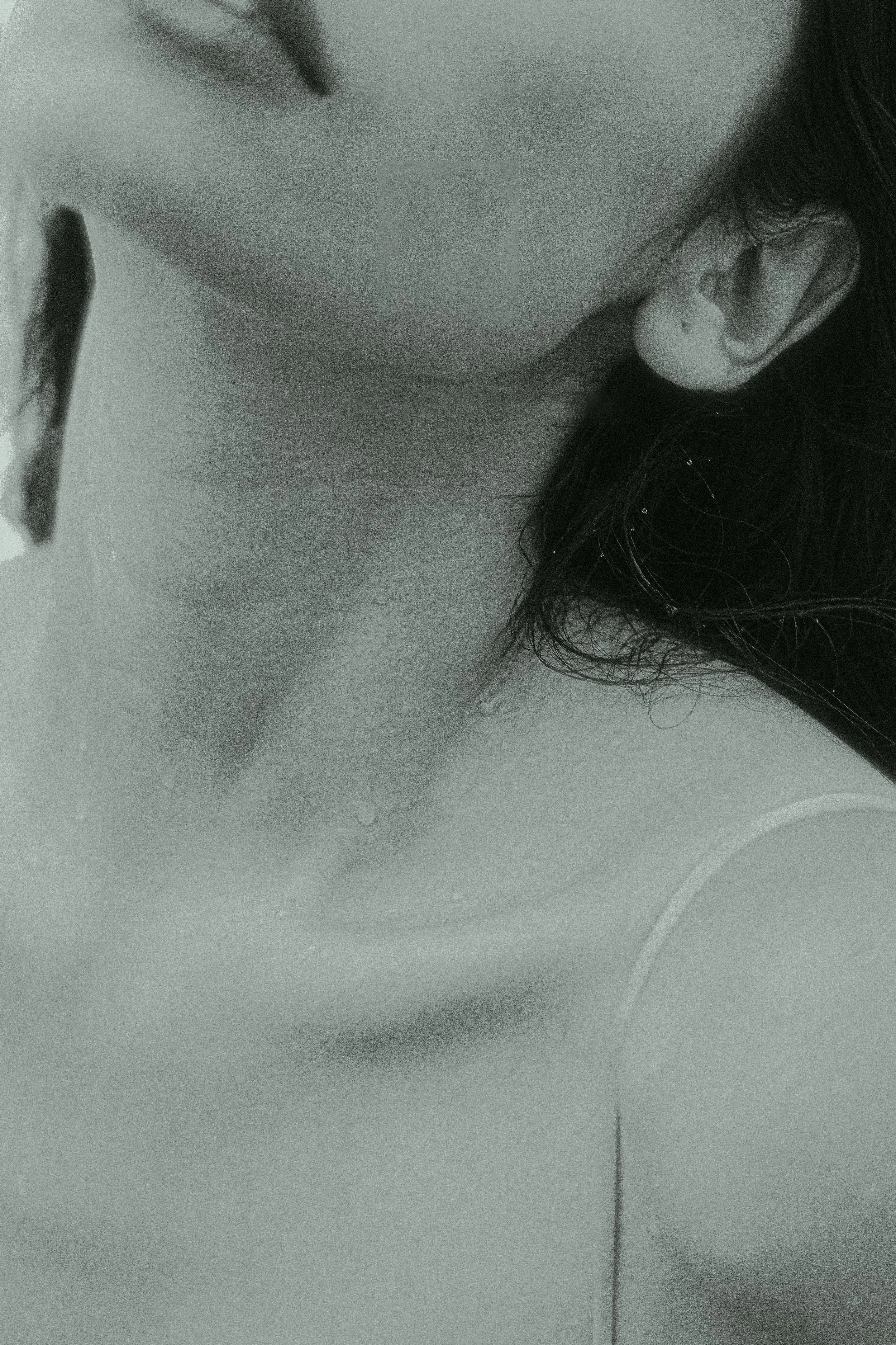 Close-up of a person in a shower, with water droplets on their skin, and wet hair covering part of their face.